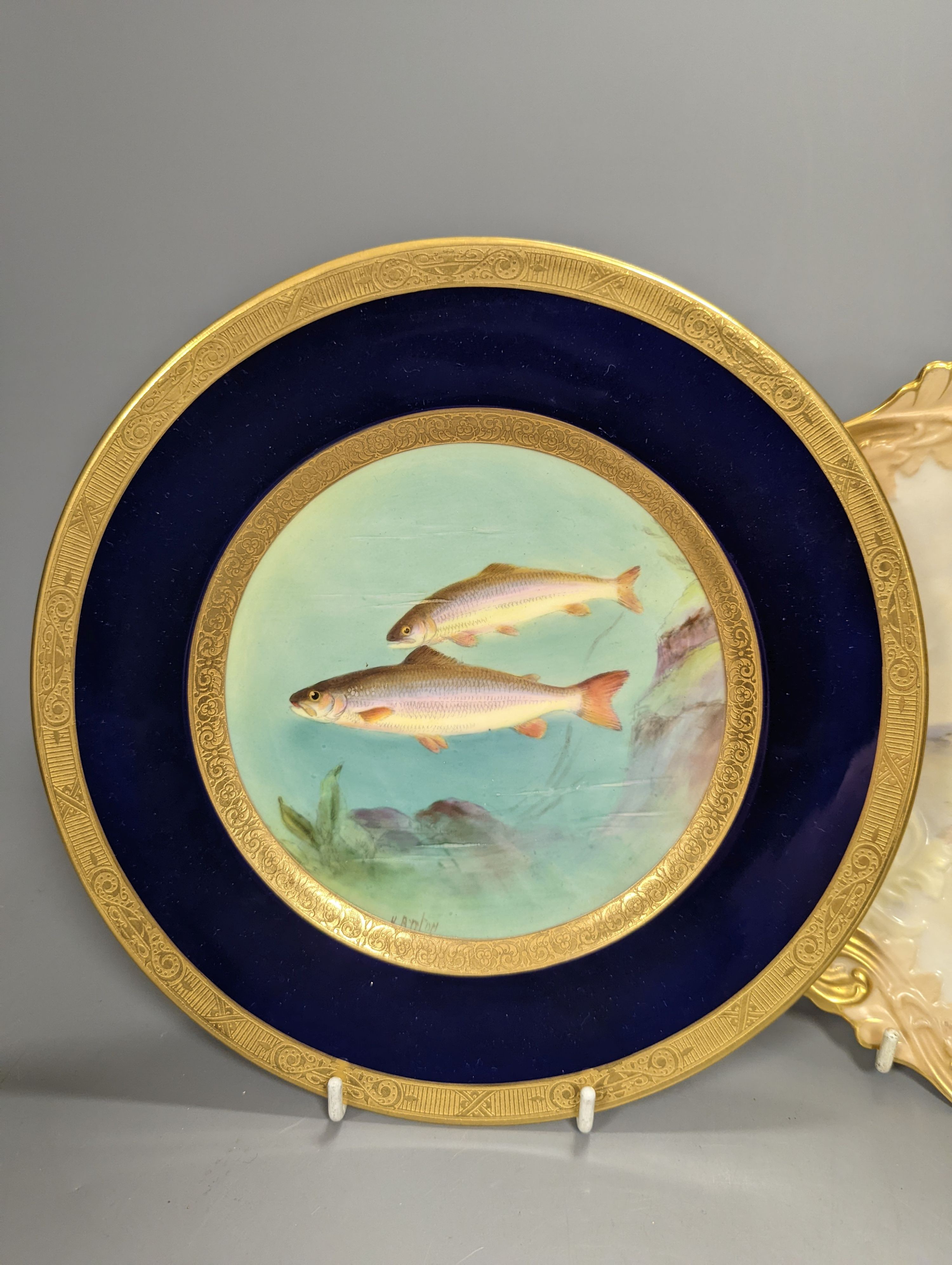 A Royal Worcester moulded plate painted with a brace of pheasants by James Stinton, not signed, date mark 1909 and a Royal Worcester fine plate painted with swimming fish, titled Char, by Harry Aryton, signed date mark f